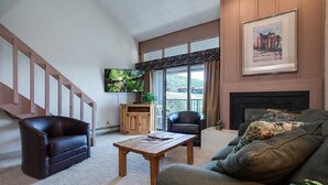 Una sala de estar con chimenea, televisor, escalera y un ventanal grande.