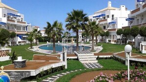 Et resort med flere hvide bygninger, palmer, en swimmingpool og en blomsterhave.