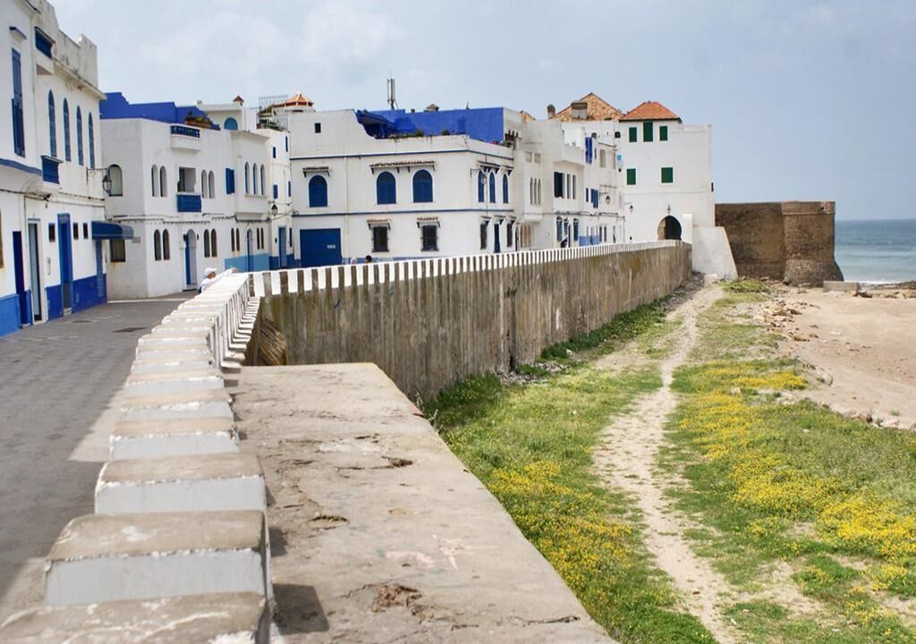 Un paseo marítimo con un muro de piedra y edificios con detalles azules.