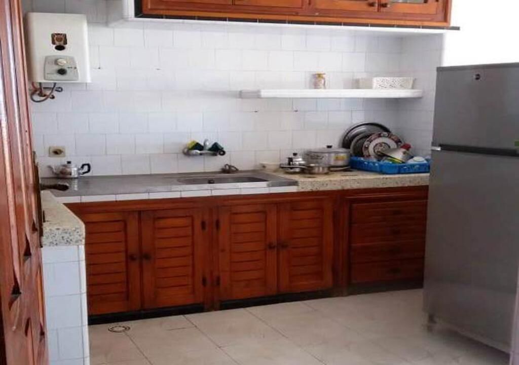 A kitchen with wooden cabinets, a stainless steel sink, and a refrigerator.