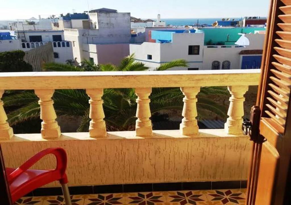 Un balcón con una silla roja, vistas a edificios y un piso de baldosas.