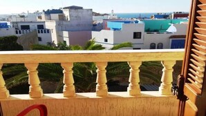 A balcony with a red chair, a view of buildings, and a tiled floor. - Apartment in Assilah 4396 (Asilah)