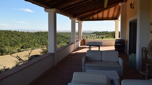 A covered outdoor seating area with wicker furniture, a table, and a view of a green landscape. - Splendid historical residence in the Lazio Maremma (Tessennano)