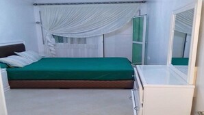 A bedroom with a green bed, white curtains, a window with a green frame, and a white bedside table. - Apartment in Martil 4421 (Martil)