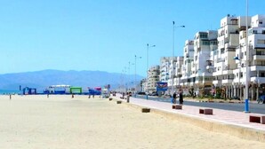 A beachside promenade with buildings, a clear sky, and distant mountains. - Apartment in Martil 4421 (Martil)