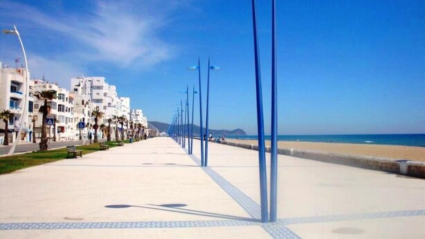 A coastal promenade with a white building, palm trees, and a clear blue sky. - Apartment in Martil 4421 (Martil)