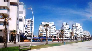 A coastal urban area with modern buildings, palm trees, and a clear sky. - Apartment in Martil 4421 (Martil)