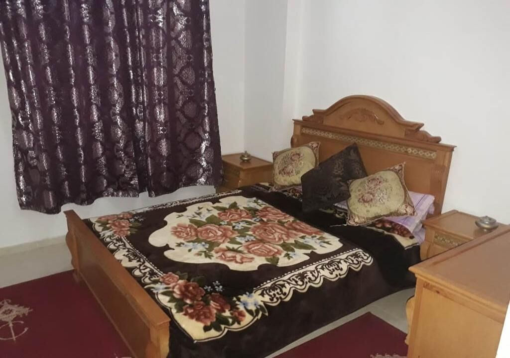 Un dormitorio con cama de madera, colcha estampada y cortina oscura.