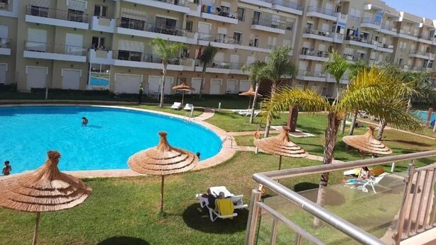 A hotel with a swimming pool, outdoor seating, and a multi-story building with balconies. - Beautiful apartment in Bouznika 4475 (Bouznika)