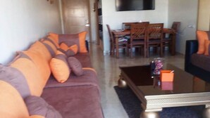 A living room with a sofa, coffee table, and a TV mounted on the wall. - Beautiful apartment in Bouznika 4475 (Bouznika)