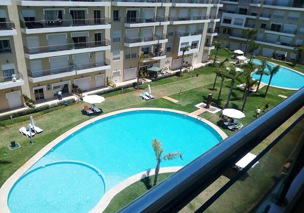 Un hotel de varios pisos con piscina, mobiliario exterior y un césped bien cuidado.