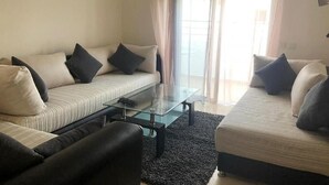 Ein modernes Wohnzimmer mit einer Sofagarnitur, einem Glastisch und einem schwarzen Teppich.