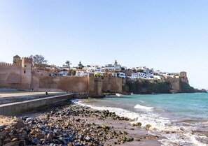 A coastal town with a fortified castle, white buildings, and a rocky beach. - Apartment in Riad Al Bahr Harhoura 4413 (Temara)