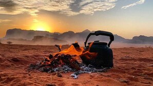 A kettle on a fire in a desert landscape with mountains in the background.