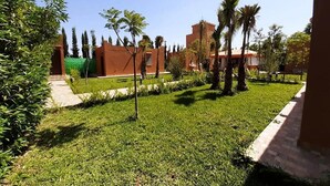 A courtyard with a well-maintained lawn, palm trees, and a brick building. - Bungalow in Marrakech 4439 (Marrakech)