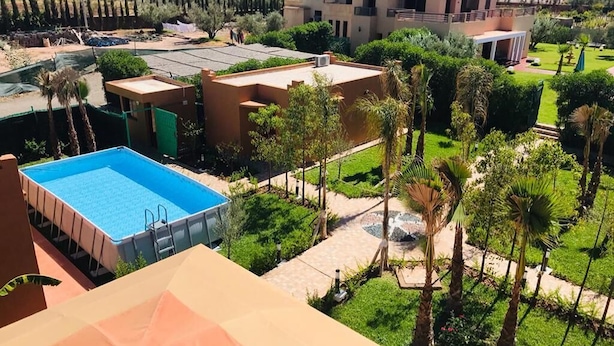 A pool area with a rectangular pool, surrounded by palm trees and a well-maintained lawn. - Bungalow in Marrakech 4439 (Marrakech)