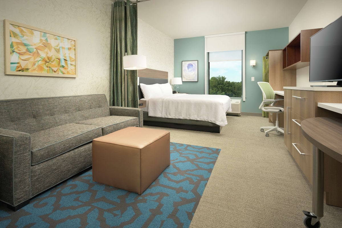 Ein Hotelzimmer mit Bett, Sofa, Schreibtisch und Fernseher.