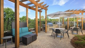 Eine Außenpatio mit Holz-Pergolen, einem Grill, einer Sitzecke und Tischen.