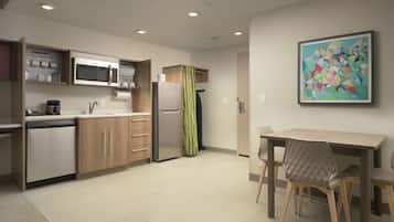 Une cuisine moderne dotée d’appareils électroménagers intégrés, un coin repas avec une table et des chaises, et un tableau abstrait aux couleurs vives accroché au mur.