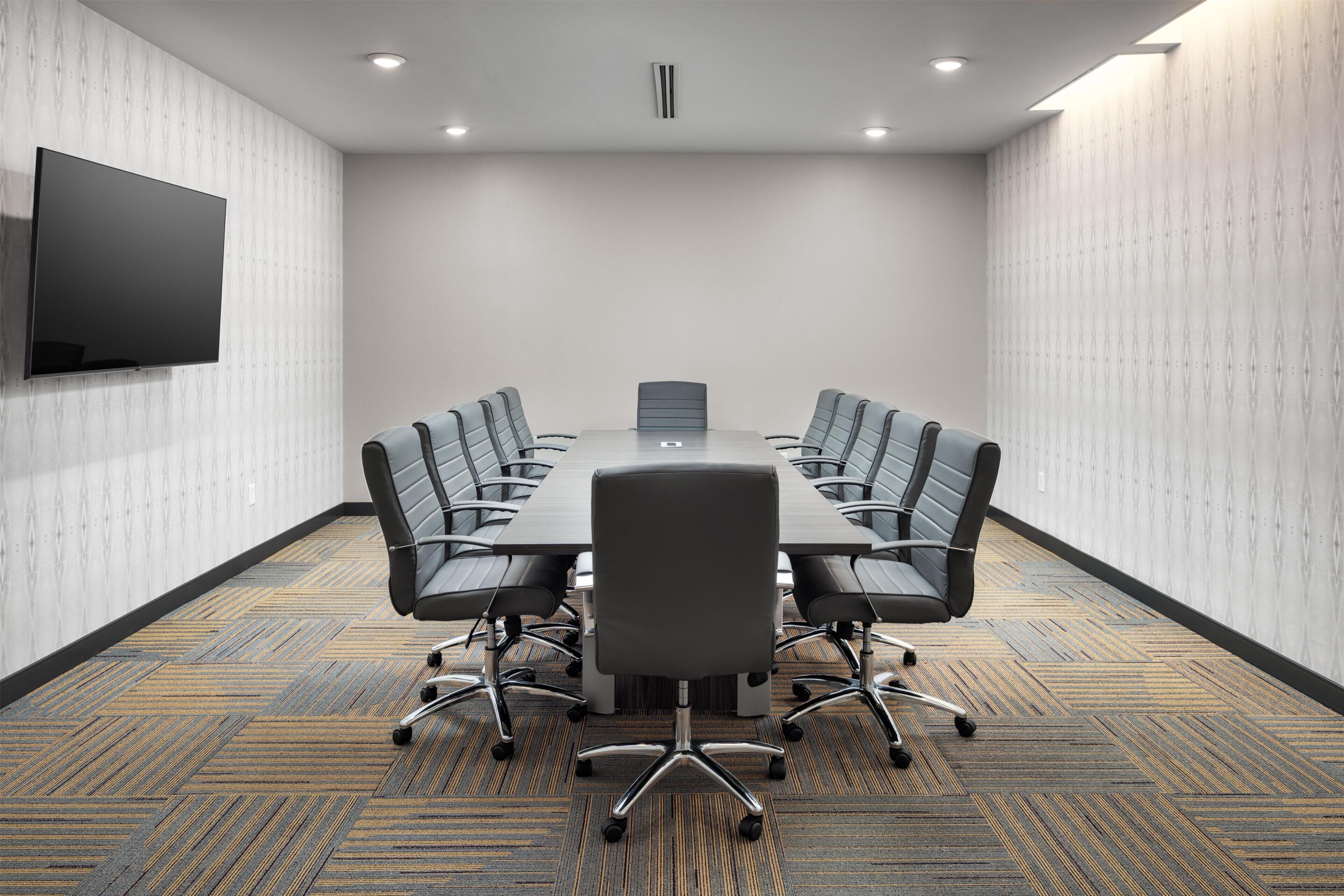 A conference room with a large table, six chairs, a flat-screen TV, and patterned carpet.