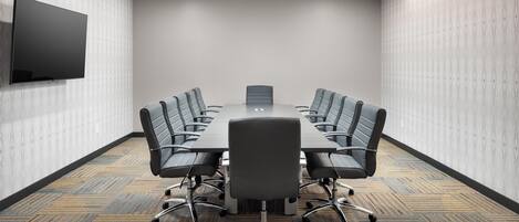 A conference room with a large table, six chairs, a flat-screen TV, and patterned carpet.