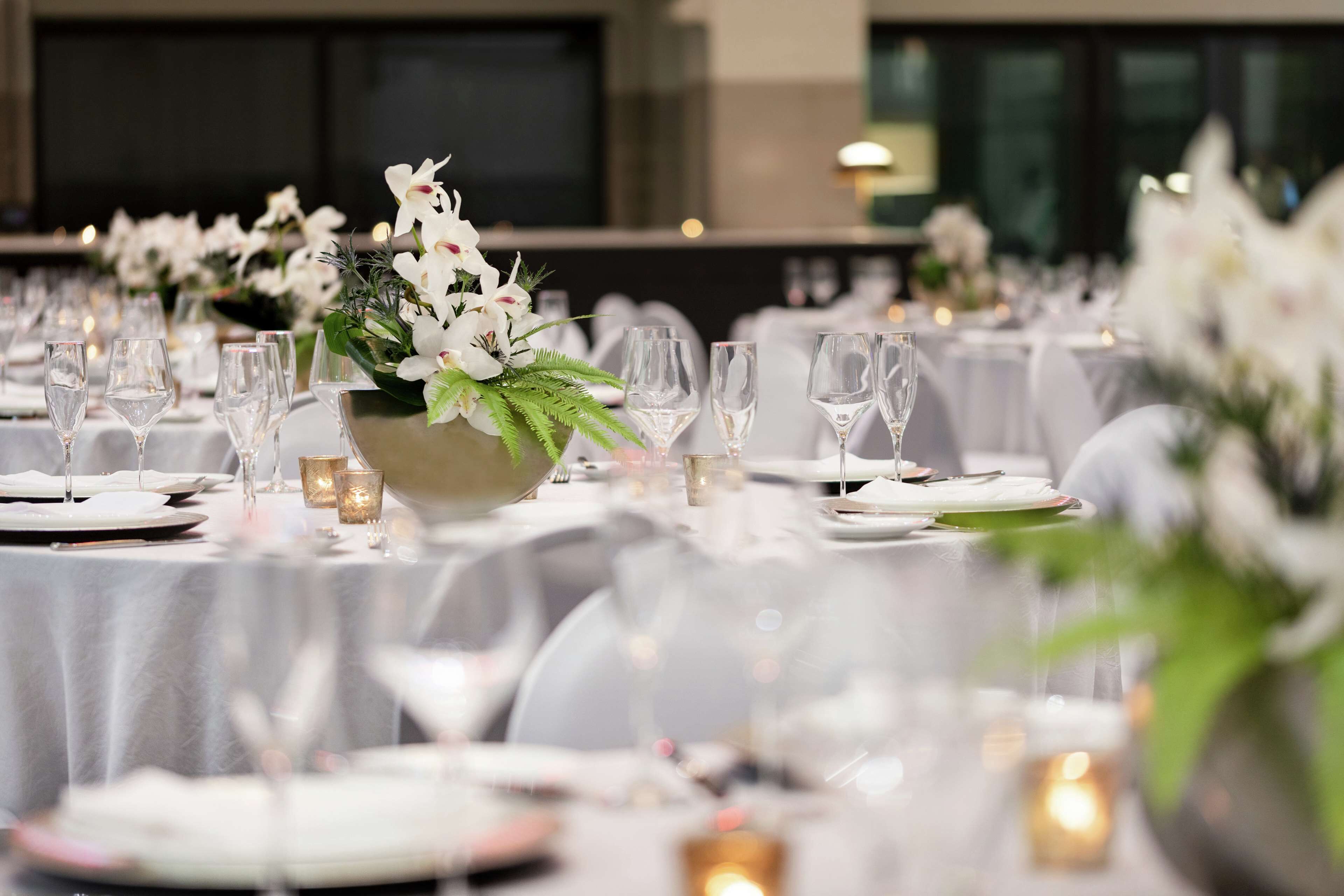 Un salón de banquetes con mesas dispuestas para un evento formal, con manteles blancos, cristalería y centros de mesa florales.