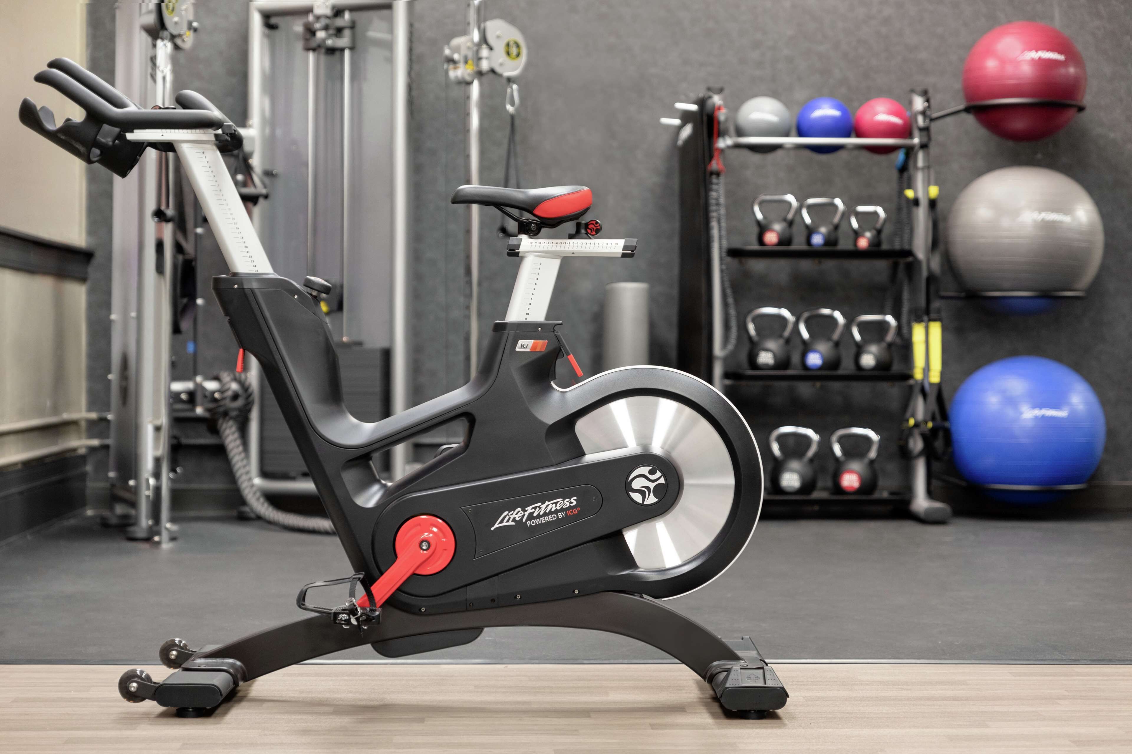 Un vélo d’appartement dans une salle de sport, avec des poids et des kettlebells en arrière-plan.