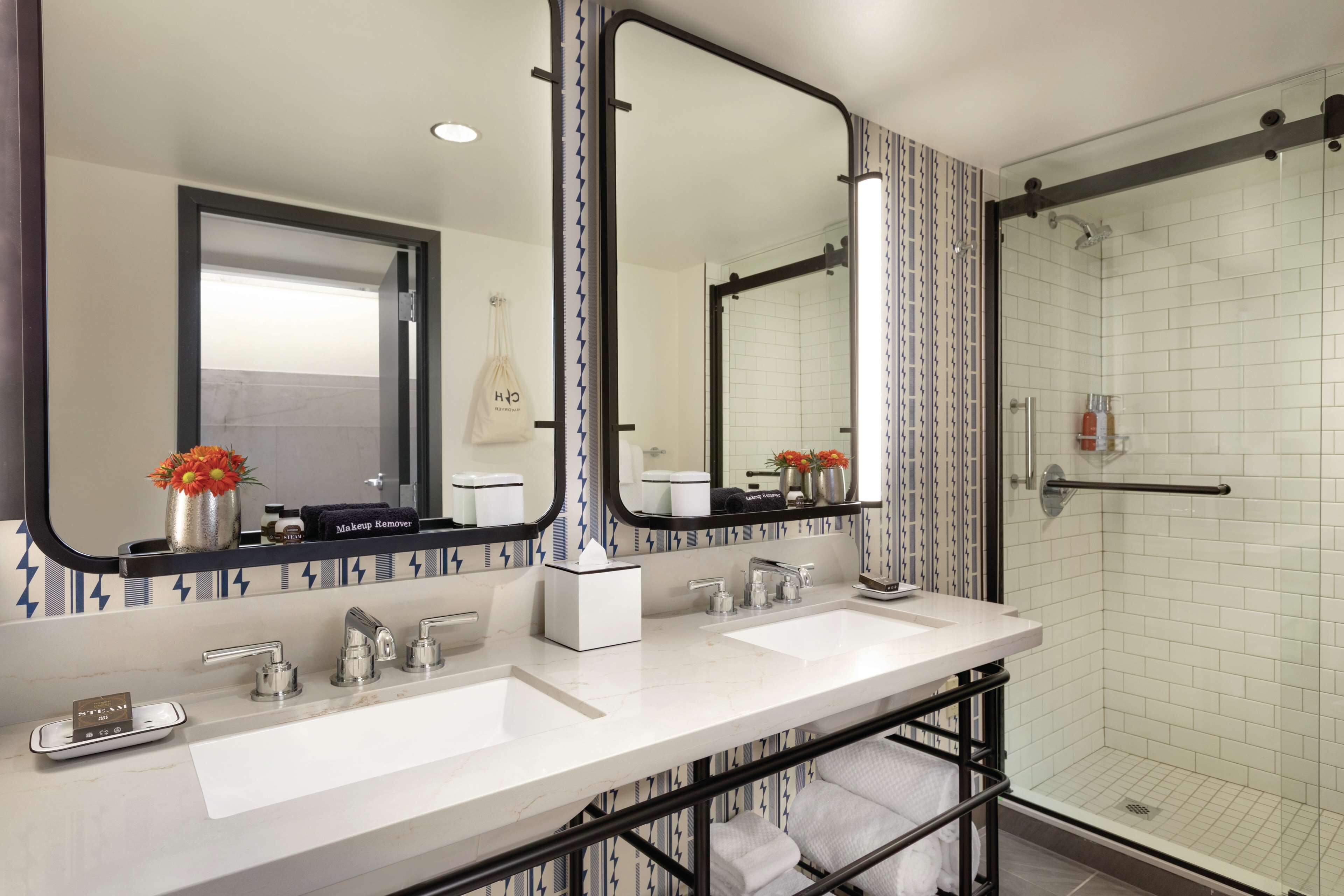 Een moderne badkamer met twee wastafels, een grote spiegel en een douche met glazen wanden.