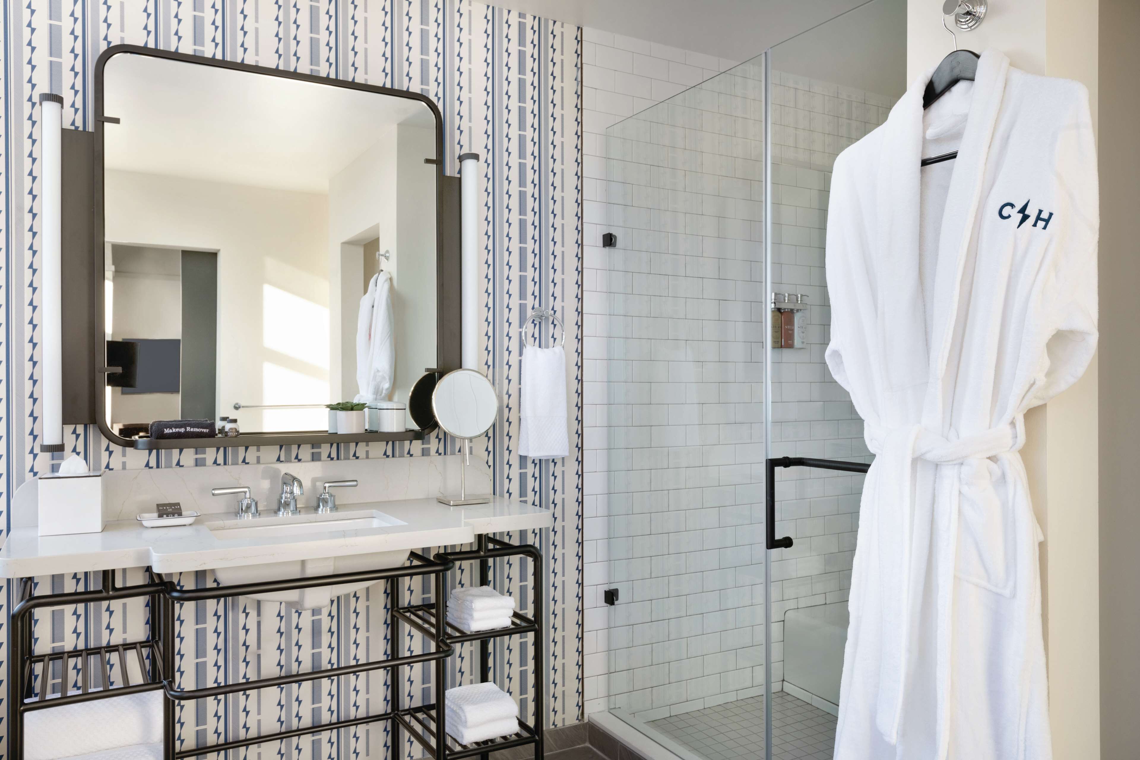 A modern bathroom with a large mirror, a shower area, and a robe hanging on a rack.