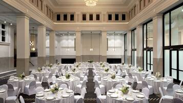 A banquet hall with round tables set for dining, white chairs, and a chandelier.