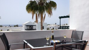 A table with two glasses of white wine, a bottle, and a menu on a balcony overlooking a beach with palm trees and white buildings. - Modern, upstairs apartment with sea view, Wifi, Air Con and U.K. TV (Puerto del Carmen)