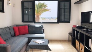 A living room with a sofa, a small table, a TV, and a window with a view of the sea. - Modern, upstairs apartment with sea view, Wifi, Air Con and U.K. TV (Puerto del Carmen)