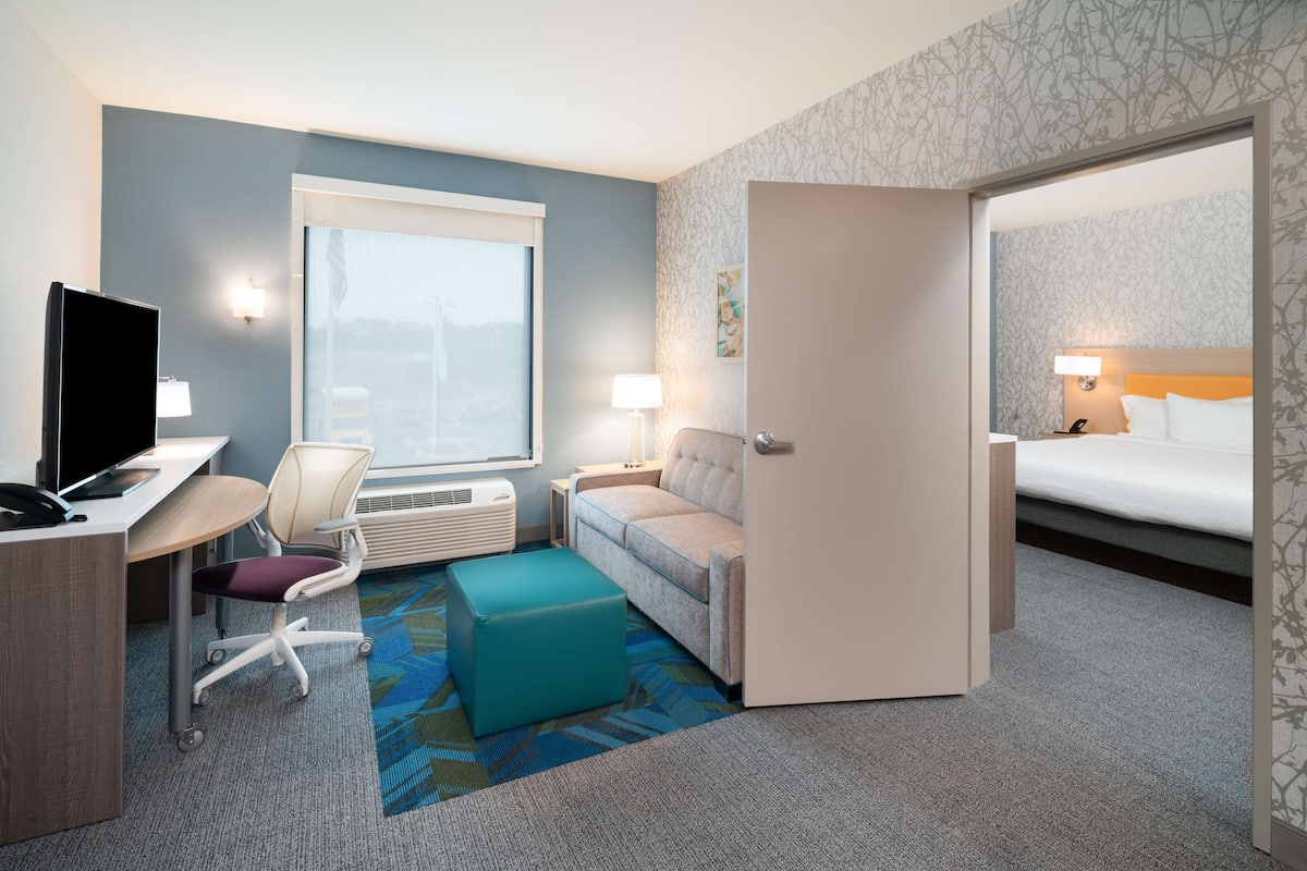 A hotel room with a desk, chair, ottoman, and a bed.