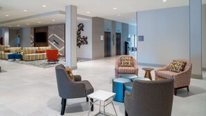 Eine geräumige Lobby mit modernen Sitzgelegenheiten, einem an der Wand befestigten Flachbildfernseher und freiem Blick auf die Aufzüge.
