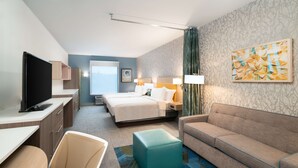 Ein Hotelzimmer mit Bett, einer Sitzecke, einem Schreibtisch mit Fernseher, einem Sessel und einem Fenster.