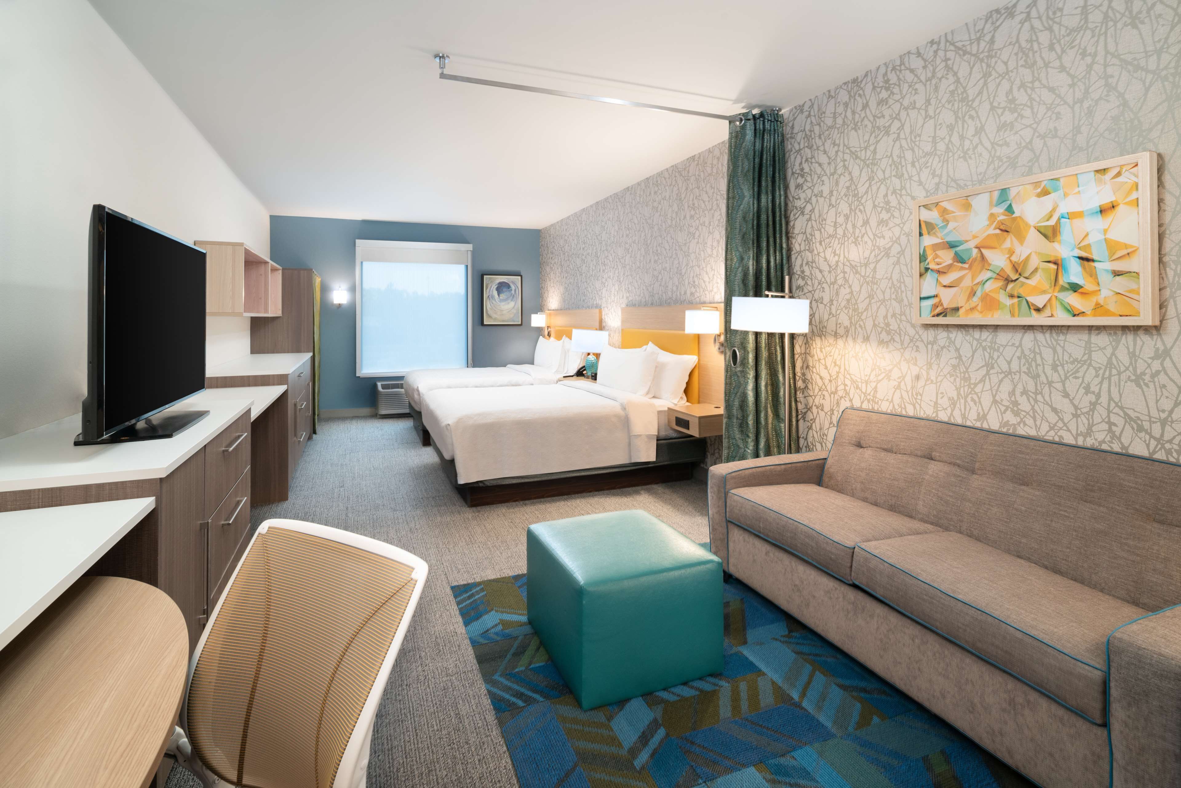 A hotel room with a bed, a sofa, a desk with a TV, a chair, and a window.
