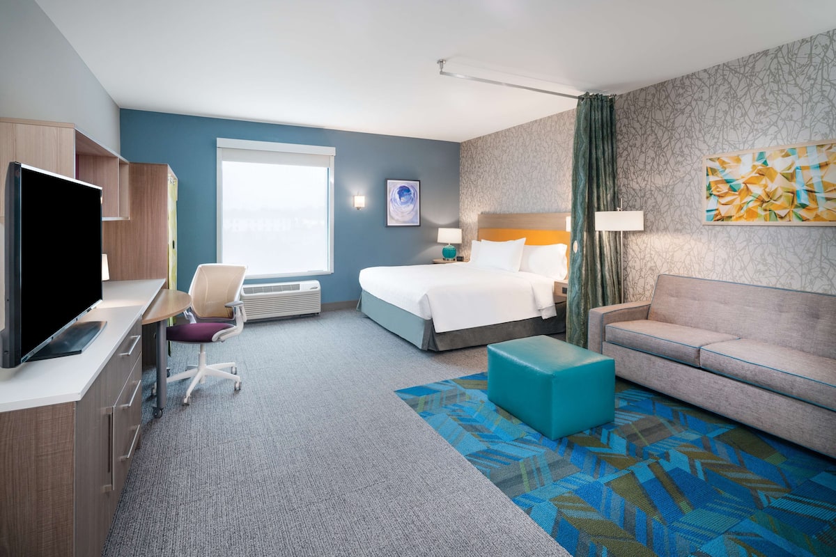 A hotel room with a bed, a sofa, a desk with a TV, a chair, and a window.