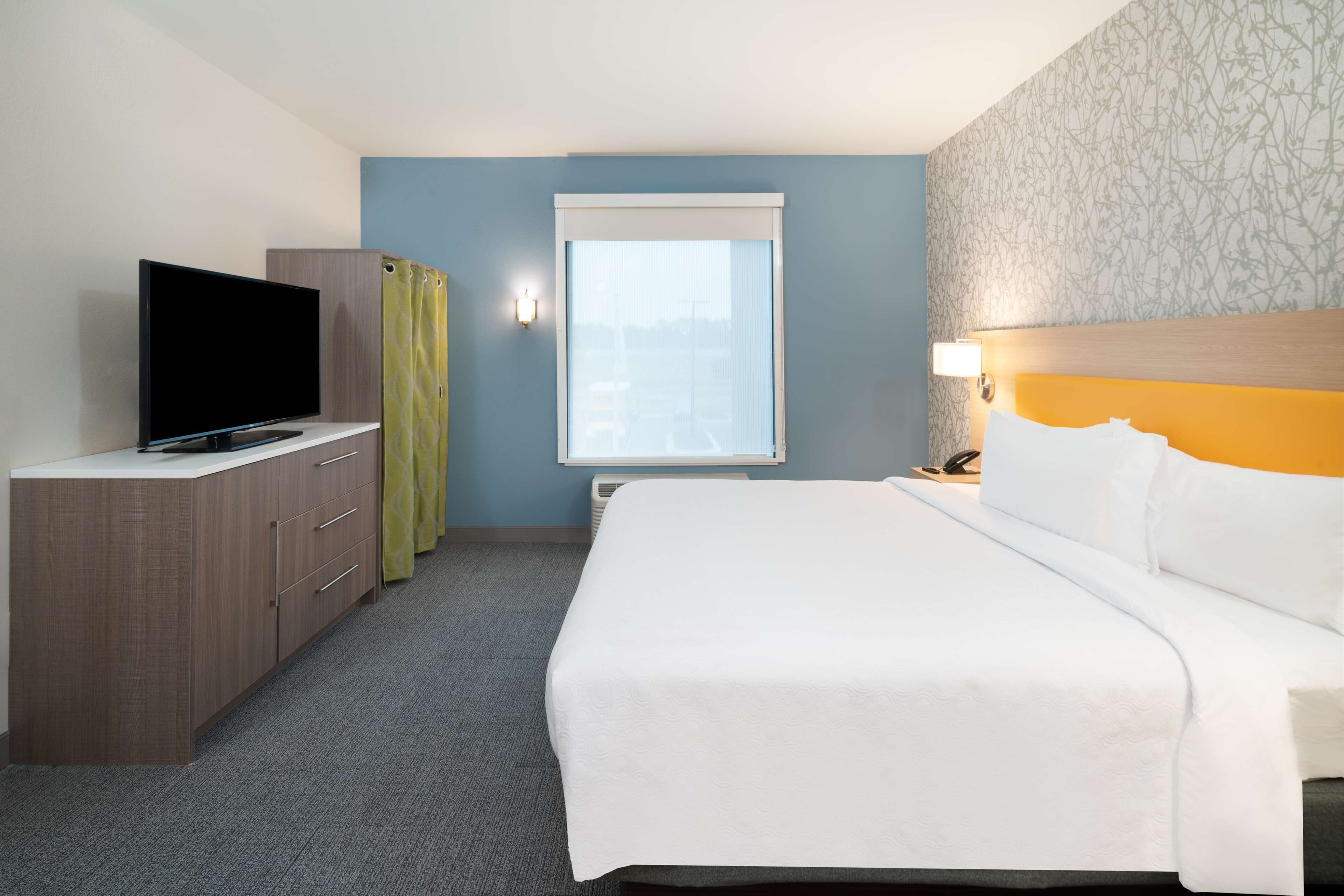 A hotel room with a bed, a television on a stand, a wardrobe, and a window with curtains.