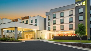 Ein modernes Hotel mit gut beleuchtetem Eingang, mehreren Etagen und einer deutlichen Beschilderung für "Home 2 Suites by Hilton".