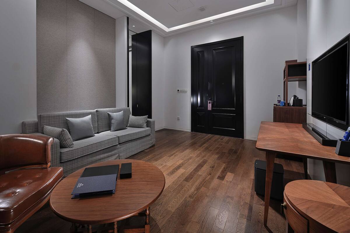 Ein modernes Wohnzimmer mit einer Couch, einem Holztisch, einem Ledersessel, einem Fernseher und einer Tür.