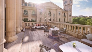 Amplia terraza al aire libre con muebles de mimbre y una torre del reloj al fondo.