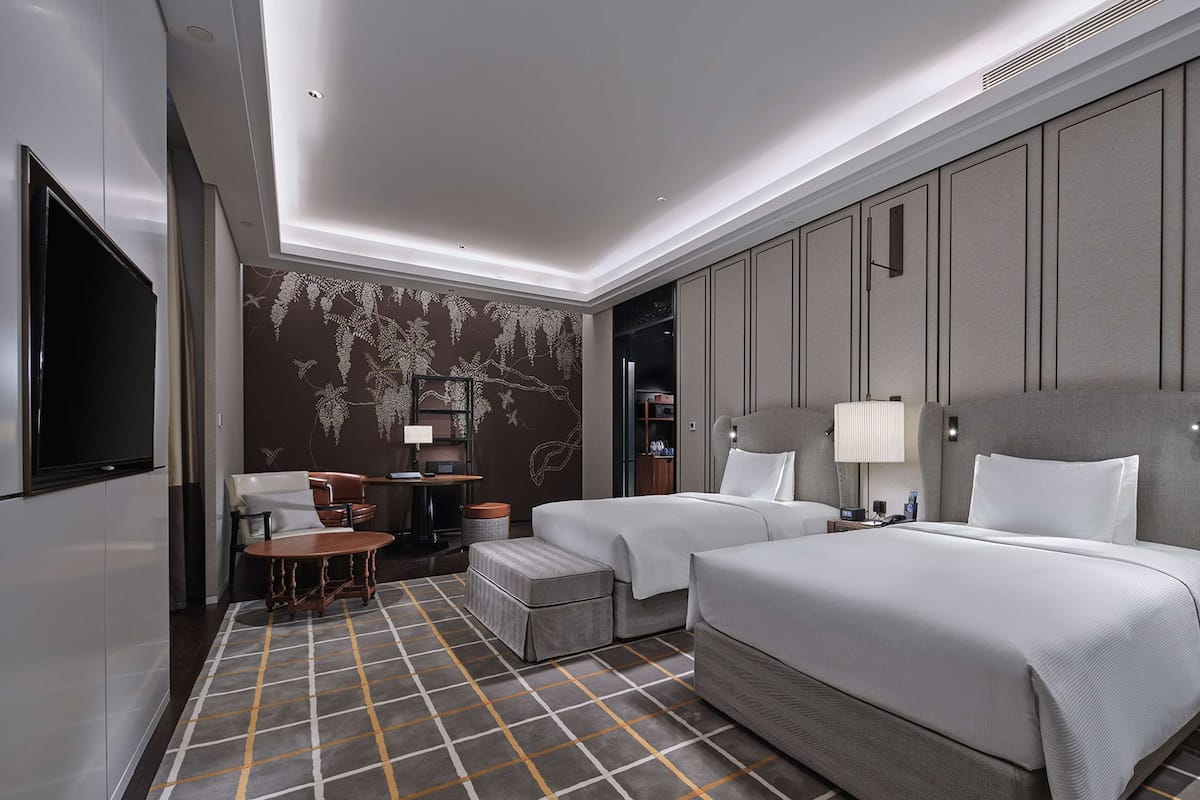 Ein modernes Hotelzimmer mit zwei Betten, einem Schreibtisch und einer Sitzecke.