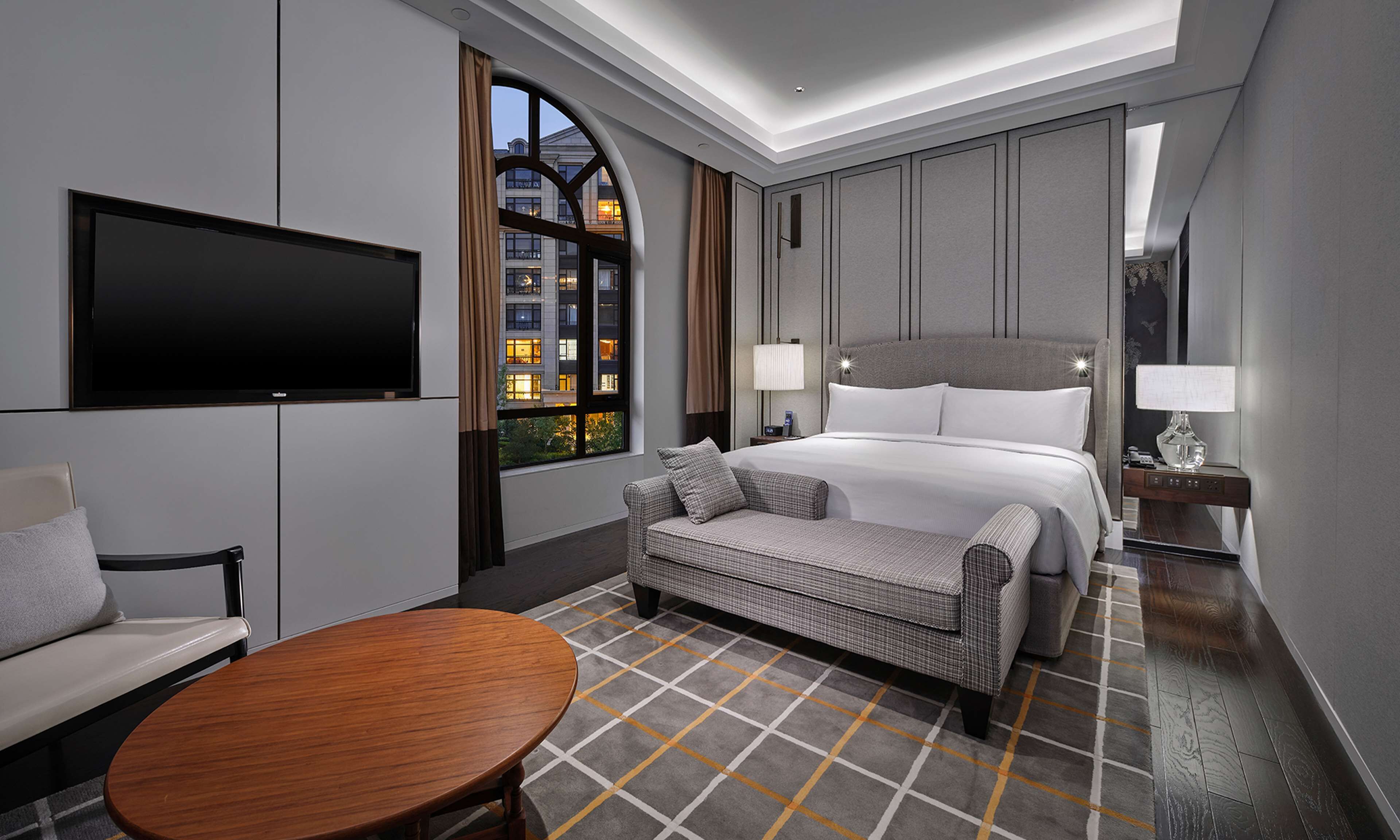 Een moderne hotelkamer met een groot bed, een televisie, een bank en een eettafel.
