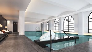Una piscina interior moderna con una barrera de cristal, amplias ventanas en arco y una zona de estar con asientos y toallas.