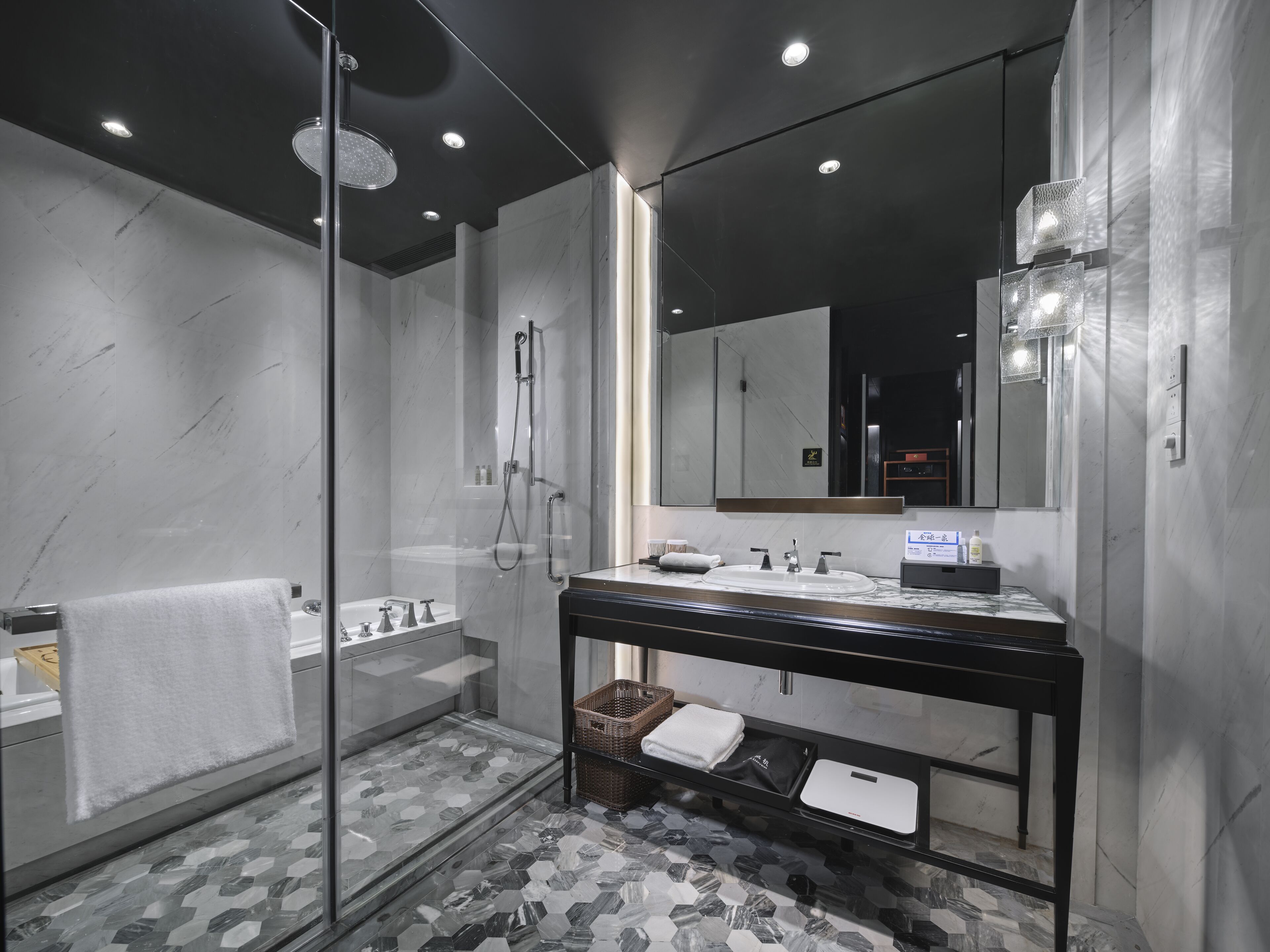 A modern bathroom with a glass-enclosed shower, a large mirror, and a marble-tiled floor.