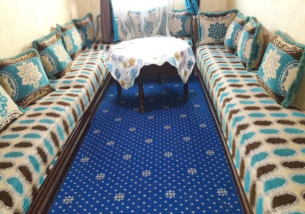 A room with a sofa set, a table with a tablecloth, and a patterned carpet.