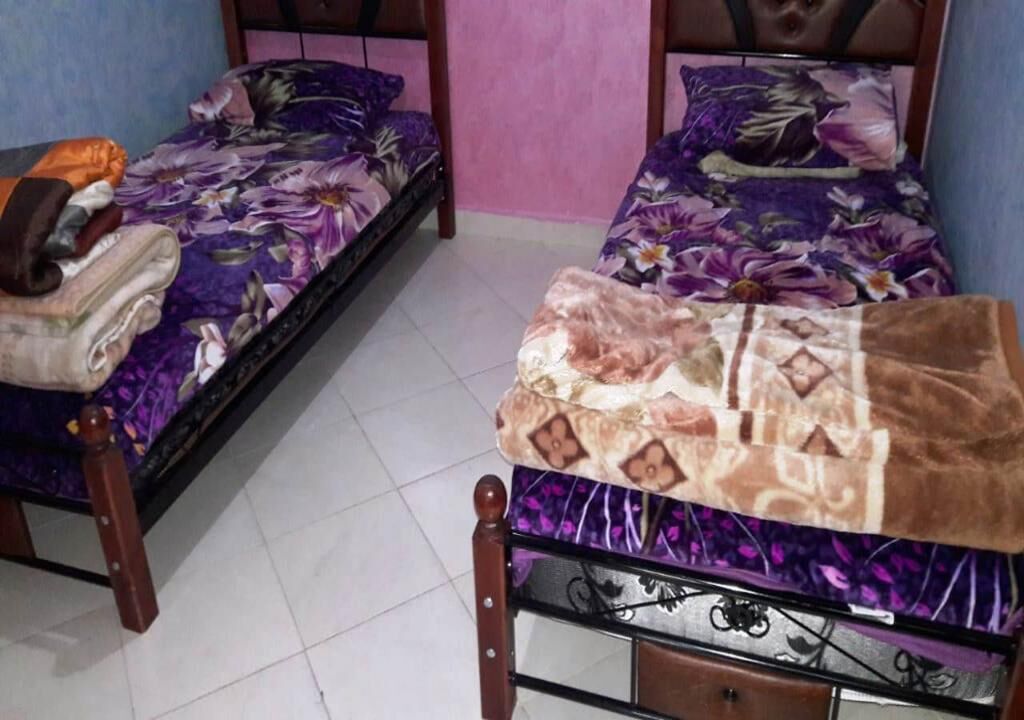 A room with two wooden beds, each with a purple floral bedspread.
