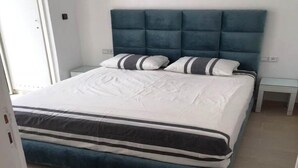 Een net opgemaakt bed met een gestoffeerd hoofdbord, witte beddengoed en gestreepte kussens.
