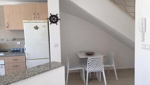 Een kleine keuken met een koelkast, een eettafel met stoelen en een decoratie van een scheepsschroef aan de muur.