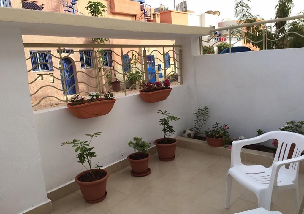 A rooftop terrace with potted plants and a white plastic chair.